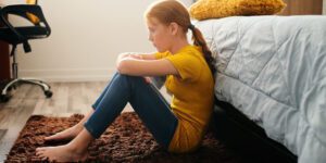 ¿un niño puede tener depresión? niña triste sentada en el suelo